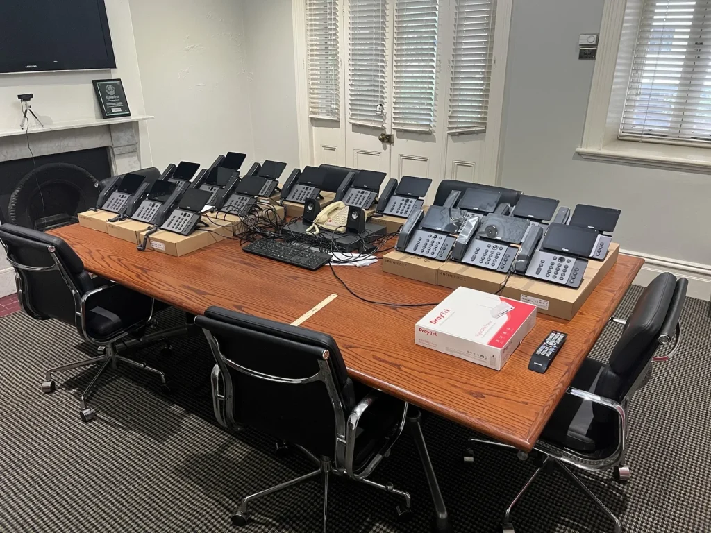 Fanvil V66 Pro desk phones and a DrayTek router laid out on a boardroom table before installation